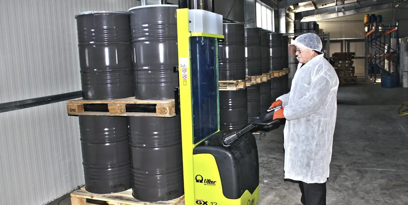 Sealed steel drums of honey on pallets, moved by an electric stacker in the warehouse.